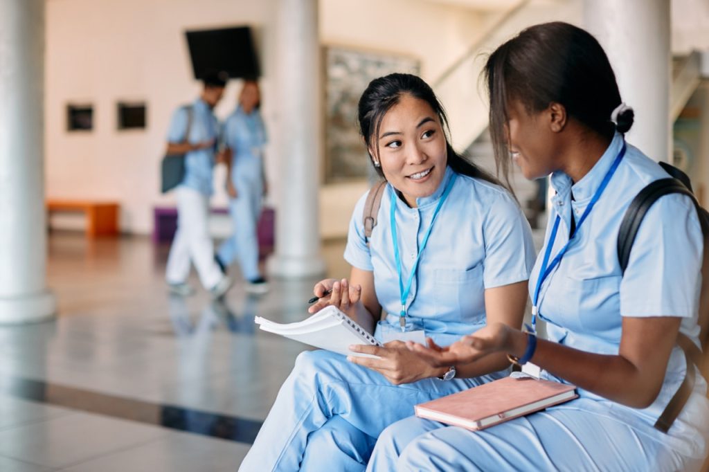 two nursing students sitting and talking while studying in hallway